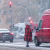 Ein Mann steht bei Schneetreiben mit einer Decke zwischen wartenden Autos und bittet um Almosen.