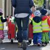 Eine Betreuerin geht mit mehreren Kleinkindern auf einem Bürgersteig.