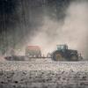 Ein Landwirt fährt mit einer Sämaschine am Traktor über ein trockenes Feld und zieht eine Staubwolke hinter sich her.  
