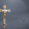 Ein katholisches Kruzifix ist vor dunklen Wolken zu sehen.