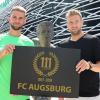 Daniel Baier, Kapitän und dienstältester Spieler, sowie Simon Asta, mit 17 Jahren jüngster FCA-Profi, präsentieren das Jubiläumslogo an der Seite der Helmut Haller-Statue.