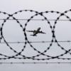 Ein Flugzeug startet - fotografiert durch Stacheldraht am Flughafenzaun.