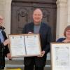 Linkes Bild: Rudolf Horner, Wolfgang Schenk und Gertrud Ehrhart (von links) präsentieren die Partnerschaftsurkunden. Schirme in den Lauinger Stadtfarben zählen zu den Gastgeschenken für Segré. Rechts Bild: Die Bürgermeister Antoine Glemain und Georg Barfuß unterzeichneten die Partnerschaftsurkunde im Mai 1988. 