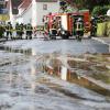 Einsatzkräfte der Feuerwehr reinigen eine überflutete und verschmutzte Straße.