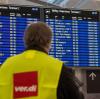 Ein Streikposten der Gewerkschaft Verdi steht am Flughafen München vor einer Anzeigetafel.