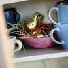 Ein Osternest mit Schokohase und Schokoladeneiern ist in einer Wohnung zwischen Geschirr im Schrank versteckt.