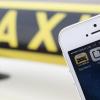 Die Handy-Apps "Uber" und "Taxi Berlin" sind auf einem Smartphone vor einem Taxi in Berlin.