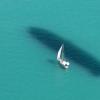 Ein Segelboot ist auf dem Bodensee unterwegs, während neben dem Boot der Schatten eines Zeppelin NT im Wasser zu sehen ist.