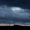 Windräder stehen bei Aitrang im Allgäu unter dichten Regenwolken hinter einem Wald.