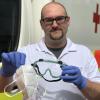 Der Hygienebeauftragte des BRK Augsburg, Philipp Eschenlohr, zeigt die Schutzausrüstung für Sanitäter mit Maske und Schutzbrille. 