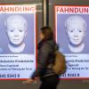 Eine Frau geht am Ostbahnhof in München an einem digitalen Fahndungsplakat vorbei.