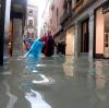 Eine  Frau und zwei Kinder waten durch das Wasser einer überfluteten Straße.