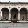 Eine Frau geht über den menschenleeren Odeonsplatz in München an der Feldherrnhalle vorüber.