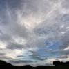 Eine aufreißende Wolkendecke zieht über eine Wiese hinweg.