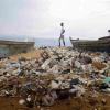 Menschen spazieren über einen mit Plastik verschmutzten Strand an der Elfenbeinküste.