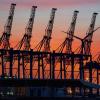 Die Sonne geht hinter den hochgeklappten Containerbrückenkränen, die normalerweise Schiffe entladen, im Hamburger Hafen unter.
