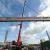 Schwerlastkräne bauen den dritten Portalkran auf, der künftig Container von einem Verkehrsmittel aufs andere heben soll. 	