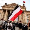 Teilnehmer einer Kundgebung gegen die Corona-Maßnahmen stehen vor dem Reichstag, ein Teilnehmer hält eine Reichsflagge mit schwarz-weiß-roten Querstreifen.