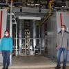 Umweltschutzbeauftragte Katharina Rochau und technischer Leiter Rainer Beinhauer jeweils vor einem der beiden neuen Blockheizkraftwerke.. 