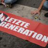 Aktivisten der Gruppe "Letzte Generation" haben sich hinter einem Banner mit ihrem Logo festgeklebt.