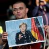 Bilanz nach einem Jahr Flüchtlingskrise: Ein Flüchtling hält ein Foto von Angela Merkel in den Händen. Was ist aus "Wir schaffen das" geworden?