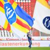 Karlsruher Fans schwenken vor Spielbeginn vor leeren Zuschauerrängen Fahnen mit der Aufschrift "KSC".