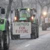 "Farmers for future" steht auf einem Schild, das an einem Traktor befestigt ist. In der Nähe von Düsseldorf fahren Bauern bei Schneefall bei einer Demonstration über eine Straße.