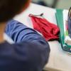 Eine Mund-Nasen-Bedeckung liegt während einer Unterrichtsstunde neben einem Mäppchen und Schulbüchern auf einem Schultisch.