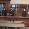 Die Verteidiger (rechts der Rechtsanwalt Bernd Scharinger) beim Prozessauftakt. Hinter der Glaswand sitzen die Angeklagten, die sich Zeitungen vor die Gesichter halten.