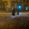 Menschen überqueren bei starkem Regen eine überschwemmte Straße in Pamplona.