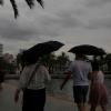 Spaziergänger mit Regenschirmen sind an der Strandpromenade von Palma unterwegs.