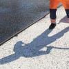 Der Schatten eines Bauarbeiters fällt auf den Boden einer Straße, die asphaltiert wird.