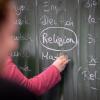 Eine Lehrerin schreibt mit Kreide einen Stundenplan mit Religionsunterricht an eine Tafel.