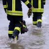 Feuerwehrleute gehen über eine überflutet Straße.