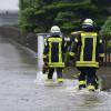 Feuerwehrleute gehen über eine überflutet Straße in Dasing.