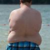 Ein übergewichtiger Junge steht an einem Badesee am Wasser. Sonne, zu viele Kilos und Vitamin D stehen in Beziehung zueinander.