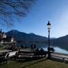 Ausflügler genießen auf Bänken das schöne Wetter am Ufer des Tegernsees.