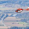 Ein Rettungshubschrauber der DRF Luftrettung fliegt durch die Luft während im Hintergrund eine mehrspurige Bundesstraße zu sehen ist.