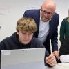 Digitalminister Fabian Mehring lässt sich von zwei Achtklässlern die erstellten Webseiten zeigen. Neben ihm schaut auch Sophie Jonke, Leiterin der ReDI School München, den Schülern über die Schulter.