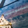 In der Fassade einer SportScheck-Filiale in der Münchener Fußgängerzone spiegelt sich ein Haus.