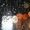Lichter von Fahrzeugen scheinen durch eine Autoscheibe, die mit Regentropfen bedeckt ist.