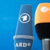Mikrofone von ARD und ZDF sind vor einer Pressekonferenz nebeneinander aufgestellt.