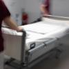 Eine Krankenpflegerin und ein Krankenpfleger schieben ein Krankenbett durch den Gang einer Station eines Krankenhauses.