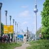 Menschen gehen und fahren an der Frankfurter Allee, während die Sonne auf den Fernsehturm scheint.