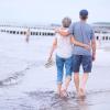 Ein Rentnerehepaar geht am Strand Arm in Arm spazieren.