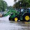 Helfer fahren mit einem Traktor Sandsäcke über eine überflutete Straße.
