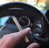 Ein Mann sitzt mit einem Joint zwischen den Fingern am Steuer eines Autos. Kiffen ist zwar inzwischen legal, Auto fahren mit THC im Blut jedoch nicht.