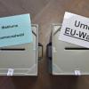 Zettel mit der Aufschrift «Wahlurne Kommunalwahl» (l) und «Urne EU-Wahl» liegen auf zwei Wahlurnen in einem Wahllokal.