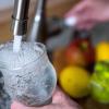 Tinkwasser läuft aus dem Wasserhahn in einer Küche in ein Glas.
