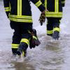 Feuerwehrleute gehen über eine überflutete Straße.